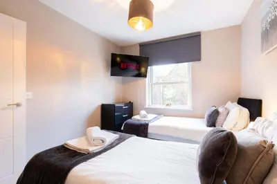 a room with two beds and a tv on the wall at Velvet 2-bedroom apartment, Conduit Lane, Hoddesdon in Hoddesdon