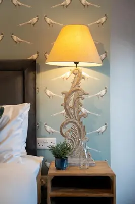 a lamp on a table in a bedroom with a bird mural at Kettleburgh Chequers in Kettleburgh
