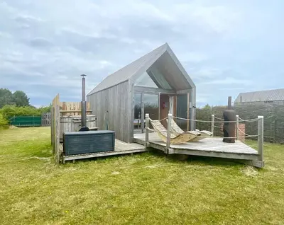 a small house with a deck and chairs on the grass at Lushna 10 Classic Suite at Lee Wick Farm Cottages & Glamping in Clacton-on-Sea