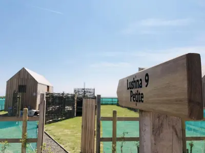 a wooden sign on a fence with a barn at Lushna 2 Petite at Lee Wick Farm Cottages & Glamping in Clacton-on-Sea