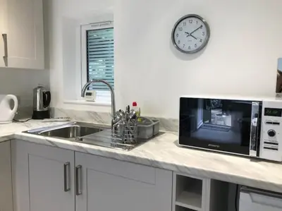 a kitchen counter with a microwave and a clock on the wall at Dolly Cottage Colchester in Mile End