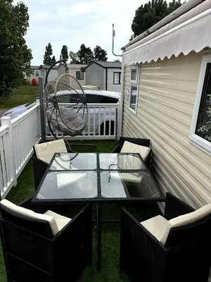 a patio with a glass table and chairs and a swing at Modern Caravan With Wifi At Seawick holiday park, Clacton on Sea 8 berth Large Decking in Clacton-on-Sea