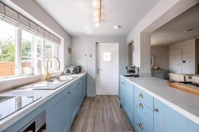 a large kitchen with blue cabinets and a window at Wonderful cottage with sun-filled terrace in Aldringham