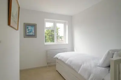 a white bedroom with a bed and a window at Hole in One in Aldeburgh