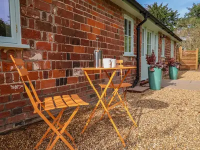 a table and two chairs next to a brick wall at Rookery Cottage in Saxmundham