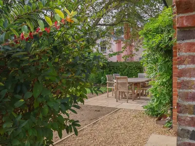 a patio with a table and chairs in a garden at Rookery Cottage in Saxmundham