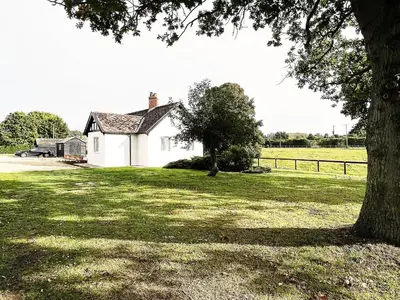 a white house in a field with a tree at Dell View by The Suffolk Cottage Collection in Bentley