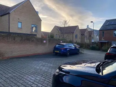 a blue car parked in a parking lot next to a brick wall at Homely, Cosy & Contemporary 4 BDR house with Garden & Parking 5 mins drive to Addenbrookes & Papworth hospitals & Bio Medical campus in Cambridge