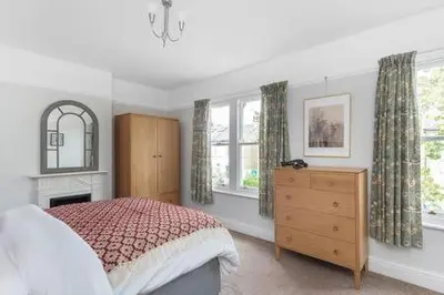 a bedroom with a bed and a dresser and windows at Victorian 2 Bedroom Home near the river Cam in Cambridge