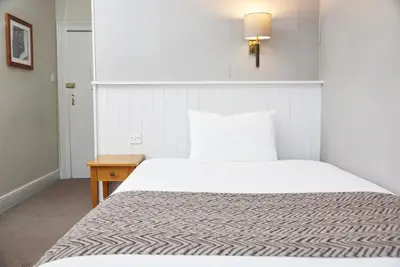 a bedroom with a white bed and a wooden table at Lamb Hotel by Greene King Inns in Ely