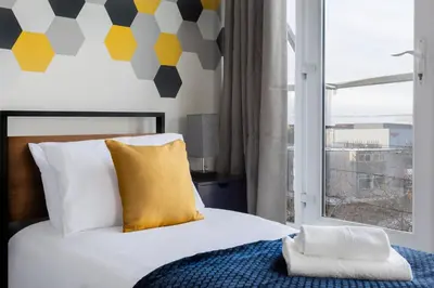 a bedroom with a bed with a yellow pillow and a window at Jade Apartments Basildon in Basildon