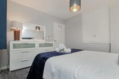 a white bedroom with a bed and a kitchen at Hurrell House in Boreham