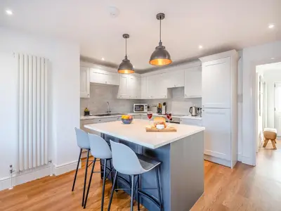 a kitchen with white cabinets and a island with bar stools at Coastal Gem in Clacton-on-Sea