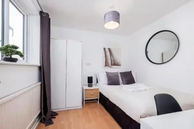 a white bedroom with a bed and a mirror at 4 Bedroom House with Parking & Garden by Cherry Inn Short Let's & Services Accomodation in Cambridge