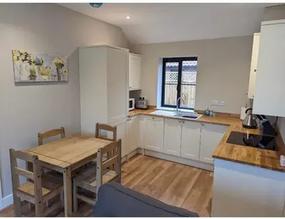 a kitchen with white cabinets and a table and a dining room at Meadow View Lodges in Bury Saint Edmunds
