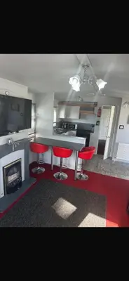 a kitchen with two red bar stools and a fireplace at Cosy Caravan near the beach in Walton-on-the-Naze