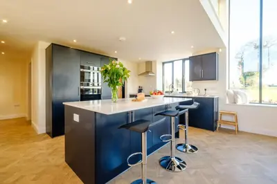 a kitchen with blue cabinets and a counter with stools at Upper Barn - a large family house by Aldeburgh Coastal Cottages in Ufford