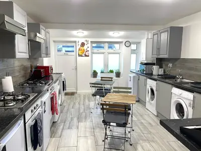 a kitchen with white appliances and tables and chairs at House - Sleeps 10 - Garden - Parking in Romford