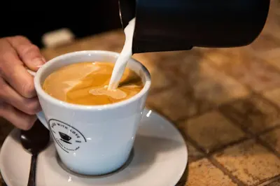 a person is pouring milk into a cup of coffee at Dragonfly Hotel Bury St Edmunds in Bury Saint Edmunds