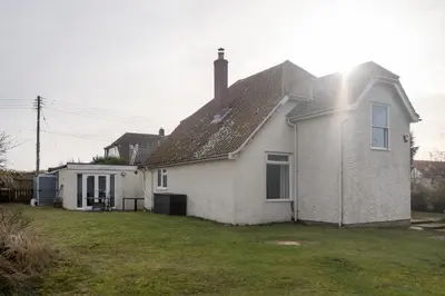 a white house with a grass yard at Fishermans Loft - A seaside house in Thorpeness with direct access to the beach - Aldeburgh Coastal Cottages in Thorpeness