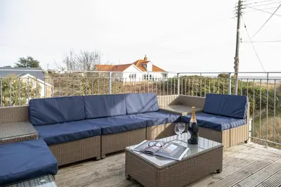 a patio with couches and a table with a bottle of wine at Fishermans Loft - A seaside house in Thorpeness with direct access to the beach - Aldeburgh Coastal Cottages in Thorpeness