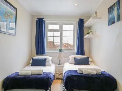 two beds in a room with blue curtains and a window at Hide and Sleep in Walton-on-the-Naze