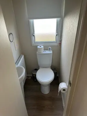 a small bathroom with a toilet and a window at 4 Bed 10 Berth Caravan Seawick Holiday Park in Saint Osyth