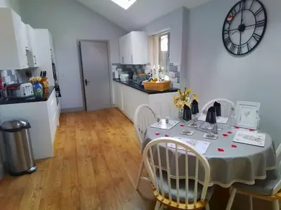a kitchen with a table with chairs and a clock on the wall at Owlhoot Annexe in Sudbury