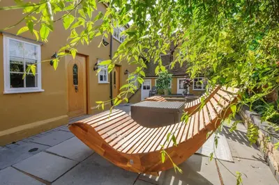 a wooden hammock in the courtyard of a house at Luxury 3 Bed Manor House With Hot Tub, Cinema Room, Sky TV in Saffron Walden