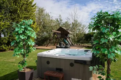 a hot tub in the middle of a yard with two trees at Deluxe 2 or 3 bed Cinema Games Room Pool Table Hot Tub in Great Sampford