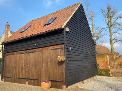 a black garage with a brown door and a red roof at The Cartlodge, Debenham in Debenham