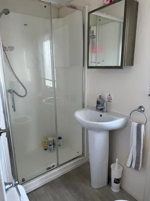 a white bathroom with a shower and a sink at D34 Steeple Bay Caravan Site in Chelmsford