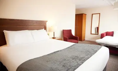 a hotel room with a white bed and a chair at White Hart Hotel by Greene King Inns in Braintree