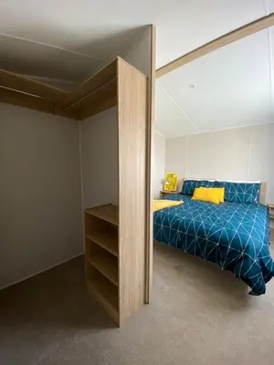 a bedroom with a bed with blue sheets and yellow pillows at VerbZen Holiday Caravan at St Osyth Beach, Clacton-on-Sea by Verb Holidays in Saint Osyth