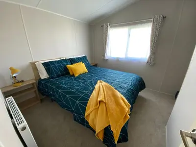 a bedroom with a blue bed with yellow pillows and a window at VerbZen Holiday Caravan at St Osyth Beach, Clacton-on-Sea by Verb Holidays in Saint Osyth