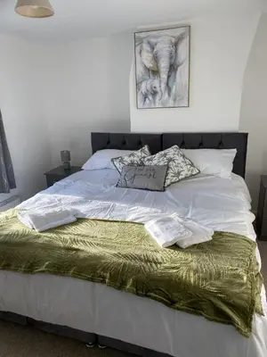 a bed with white sheets and a green blanket at Charming 3 bedroom flint cottage in Lakenheath