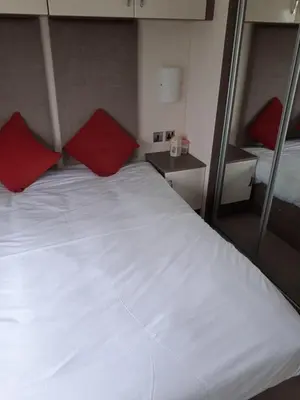 a bedroom with a white bed with two red pillows at 3 Bedroom caravan St osyth beach holiday park with free WiFi and parking in Great Clacton