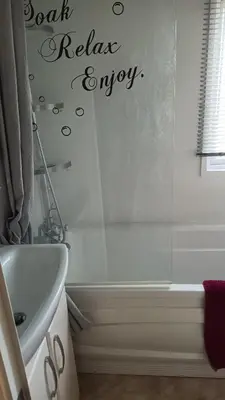 a bathroom with a bath relax enjoy sign on the wall at 3 Bedroom caravan St osyth beach holiday park with free WiFi and parking in Great Clacton