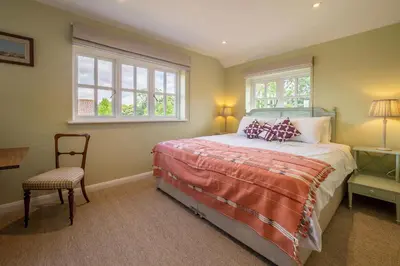 a bedroom with a bed and a chair and windows at Foxhole Cottage 8 in Stowmarket