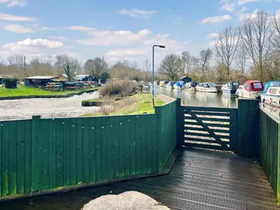 a green fence next to a river with boats at Island Lodge - Uk46767 in Little Baddow