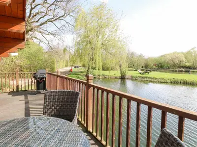 a deck with a table and chairs and a river at Heron Lodge in Langham