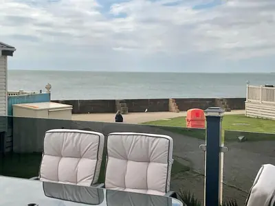two white chairs sitting on a balcony overlooking the ocean at 2 bedroom Mini Lodge Caravan at Coopers Beach Holiday Park in East Mersea