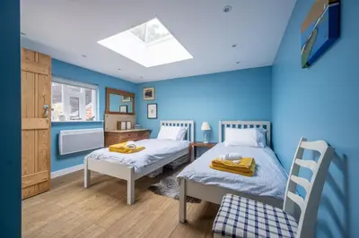 two beds in a room with blue walls and a skylight at Myrtle Cottage 4 in Friston