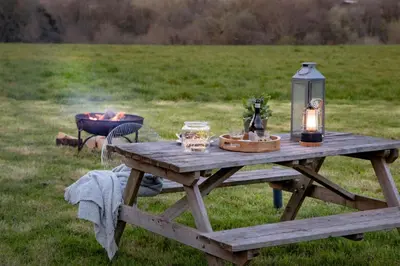 a picnic table with a lantern and a fire in a field at Swallow - Sweffling Hall in Rendham