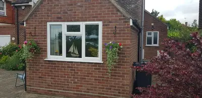 a window on the side of a brick house with flowers at Mermaid Cottages in Frinton-on-Sea