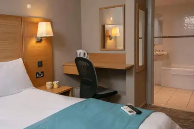 a hotel room with a bed and a desk and a bathroom at Best Western Heath Court Hotel in Newmarket