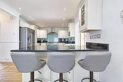 a kitchen with white chairs and a black counter top at LMV Property - Modern Luxury Family Home in Theydon Bois With London Skyline Views in Theydon Bois