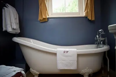 a white bath tub in a blue bathroom with a window at Ravenwood Hall Hotel in Bury Saint Edmunds
