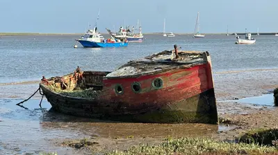 an old boat sitting on the shore in the water at Cosy 2 bed cottage in beautiful Orford in Orford