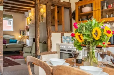 a table with a vase of flowers and wine glasses at Brimming with Medieval charm - Weavers Cottage in Lavenham